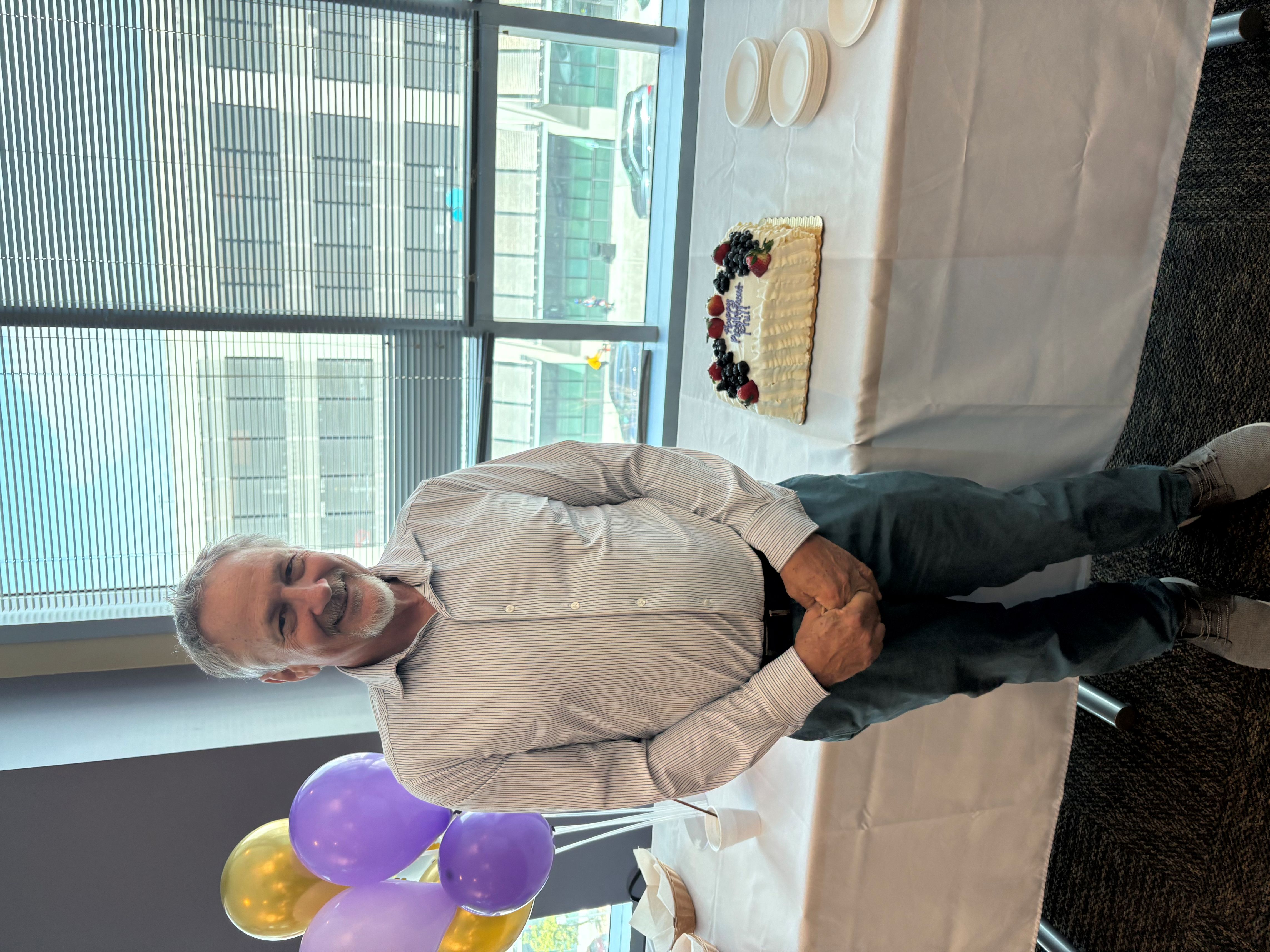 Dr. Wilson stands smiling next to a cake that has "Happy Retirement Phil" written in purple icing.
