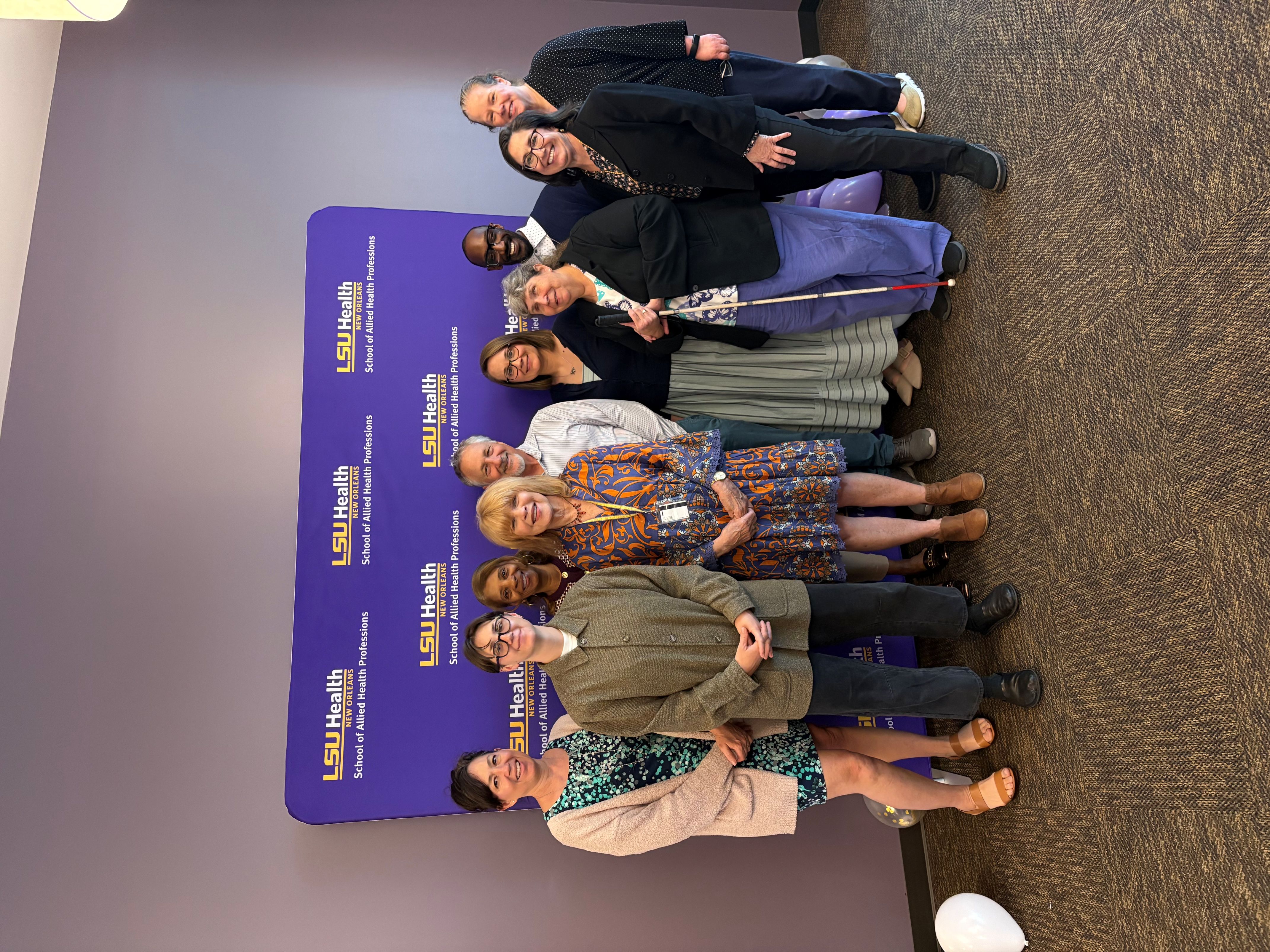 Several HDC staff and faculty smile with Dr. Wilson in front of LSUHSC School of Allied Health Professions banner.