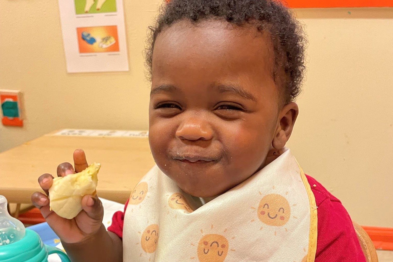 Toddler wears bib and smiles while eating a banana.