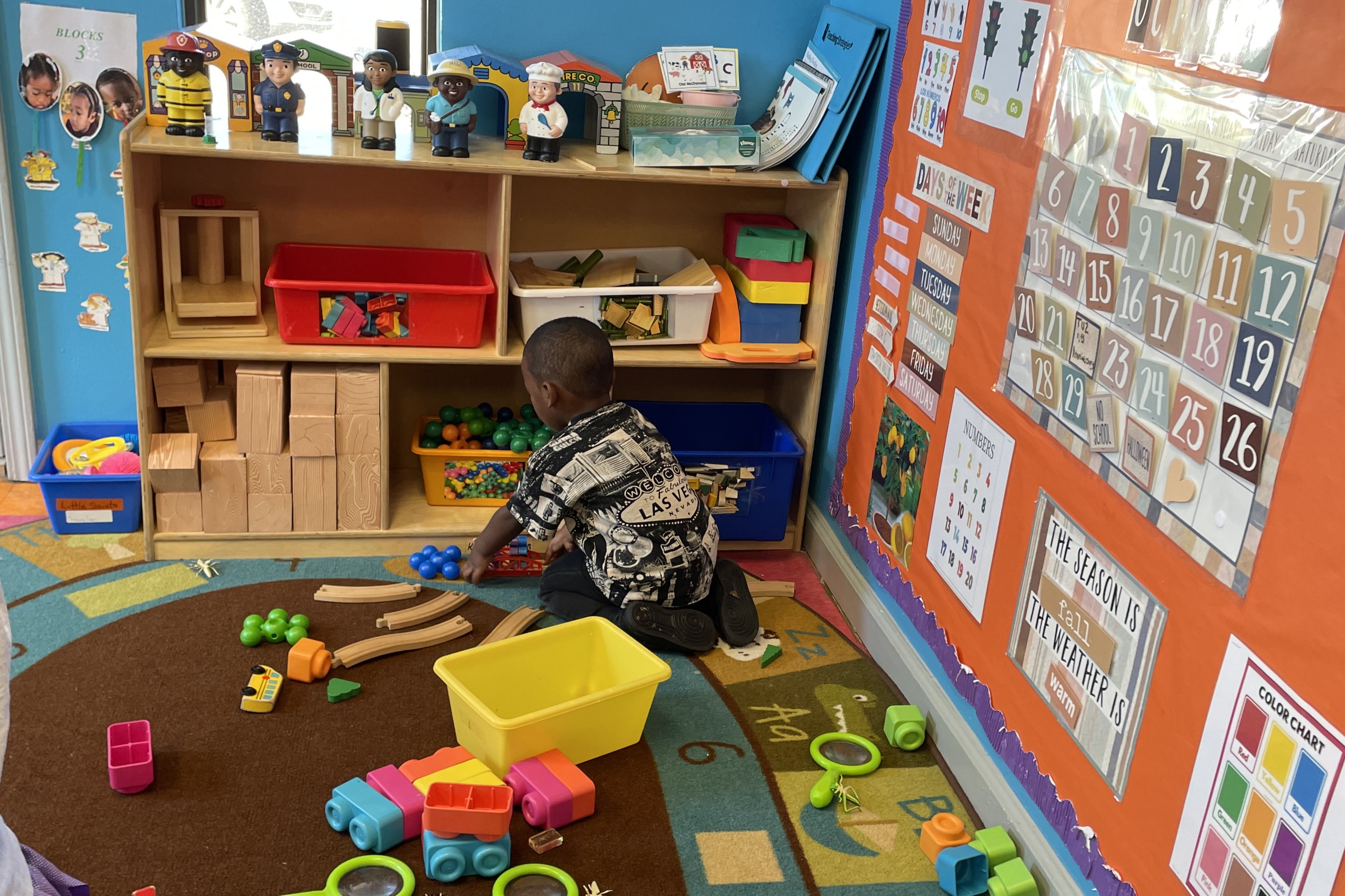 Toddle plays with train tracks in classroom.