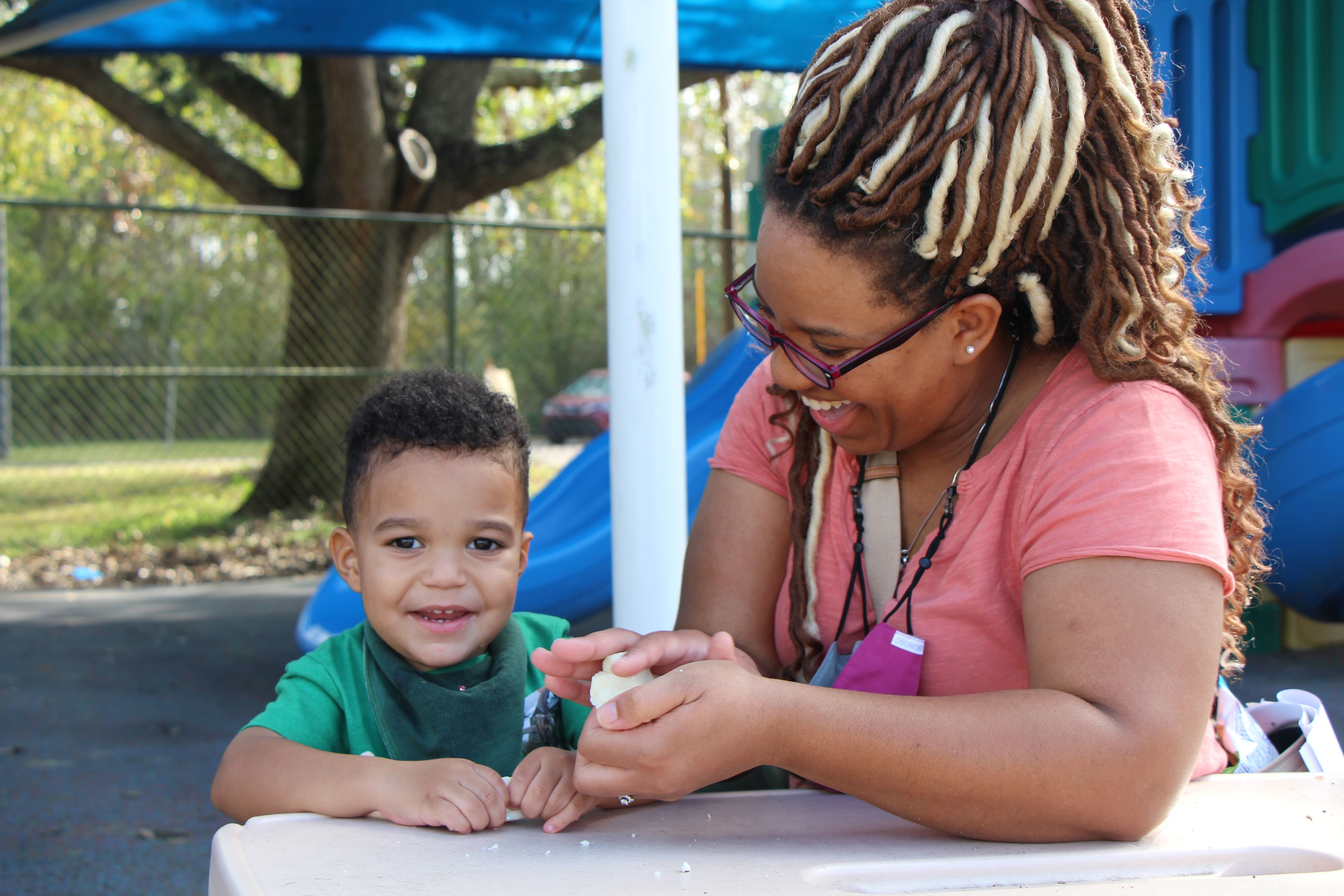 Mother plays with toddler at park bench.