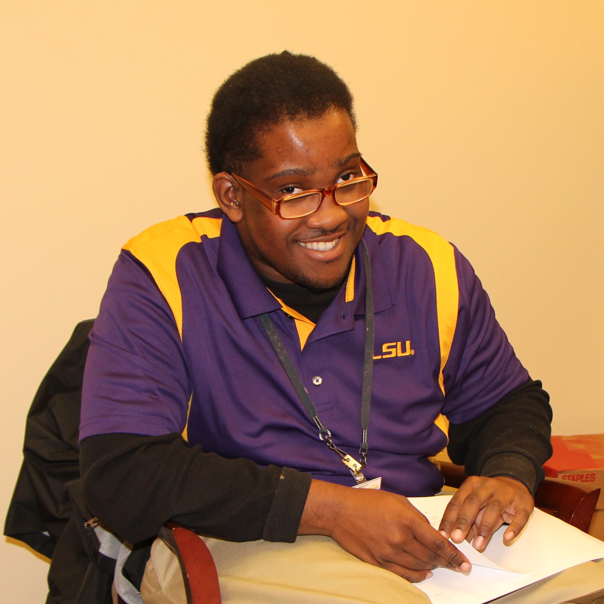 Young man wearing eyeglasses and a collared LSU shirt smiles while working in an office.