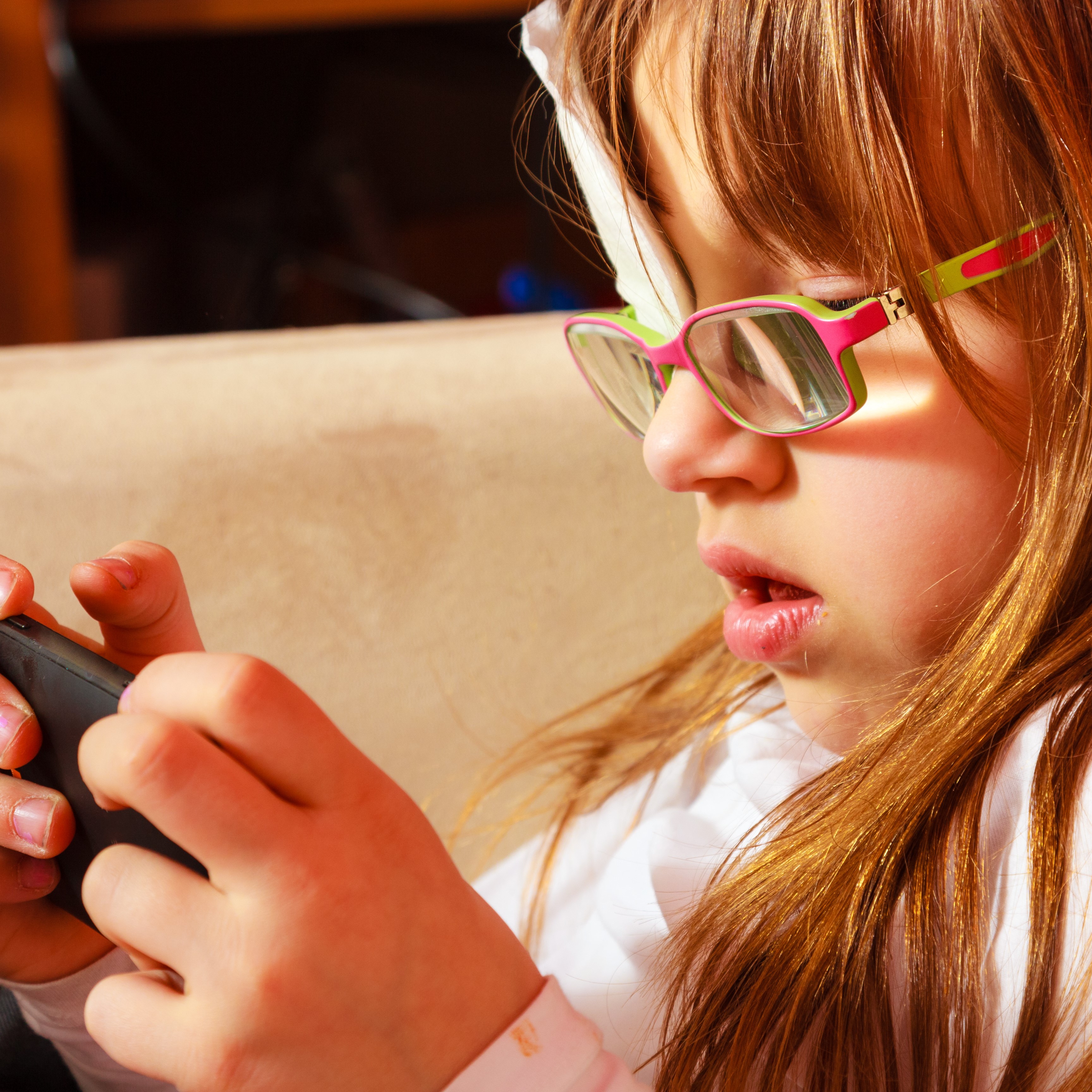 girl child in glasses and wearing an eyepatch playing games on smartphone at home
