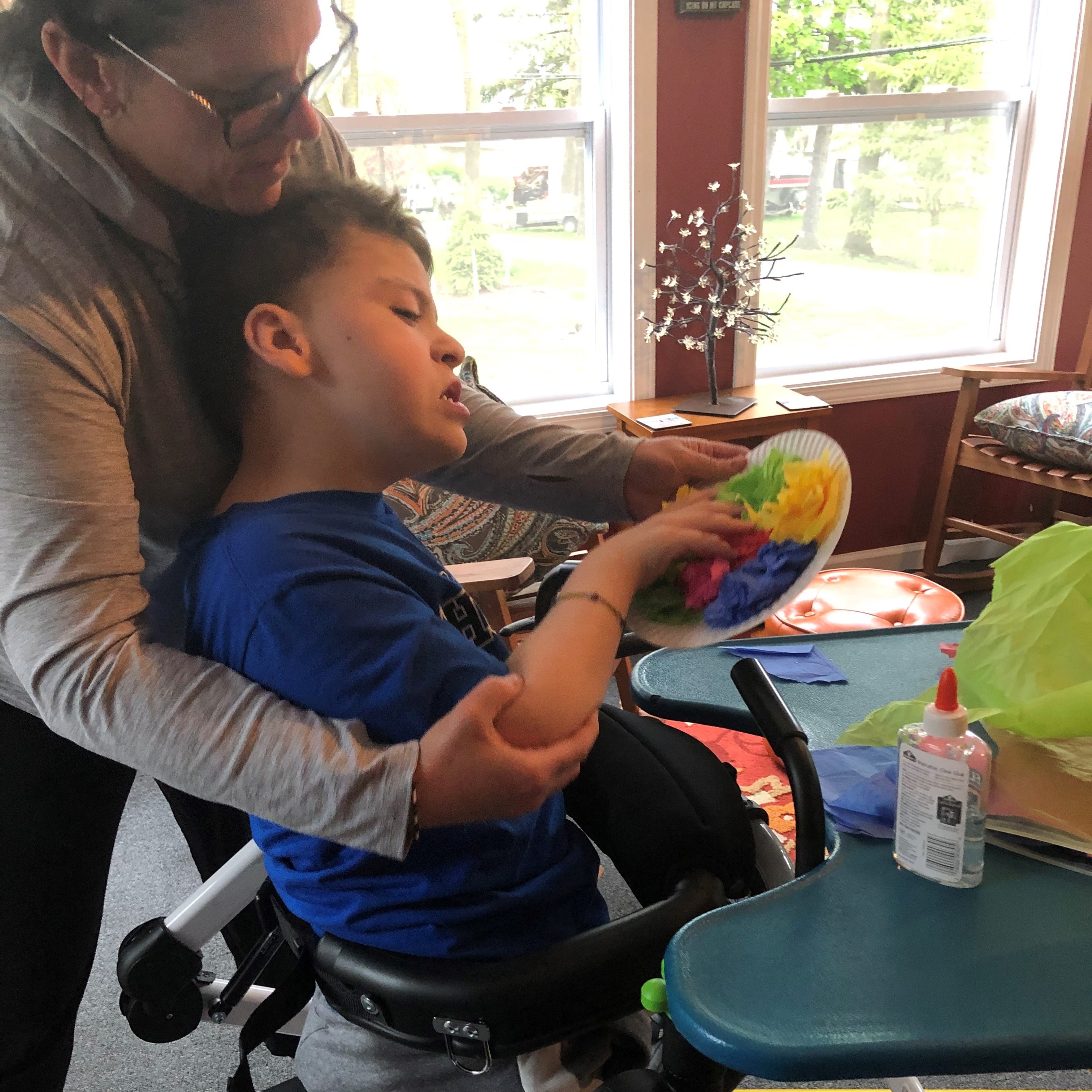 Young boy in wheelchair fingerpainting with assitance from art teacher.