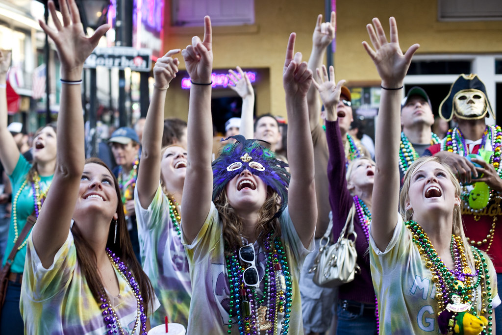 Four women wearing masks reach up to float to ask for Mardi Gras beads. 