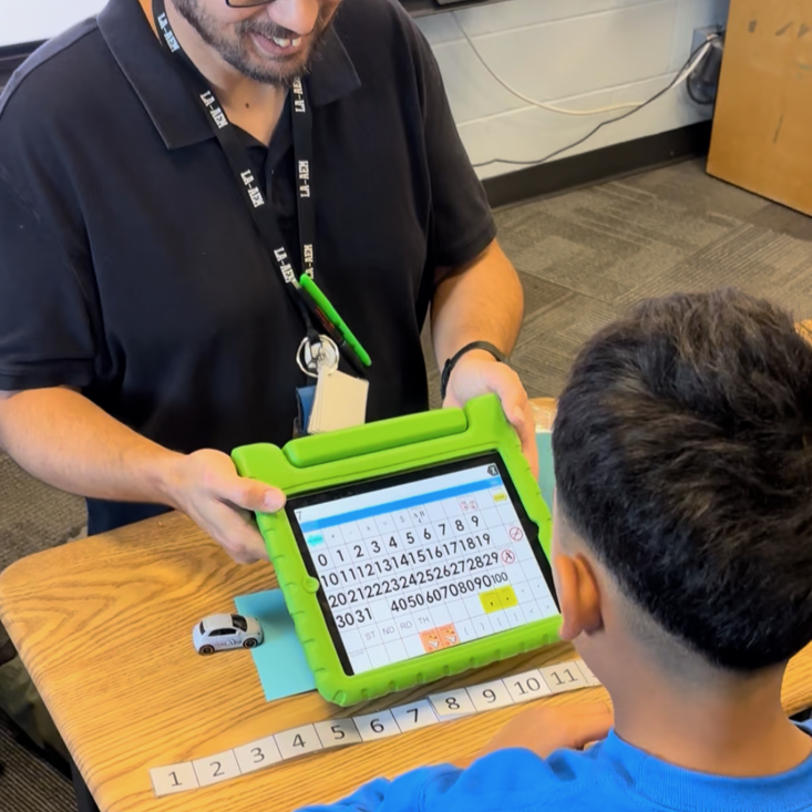 Teacher helps with communication device showing various numbers