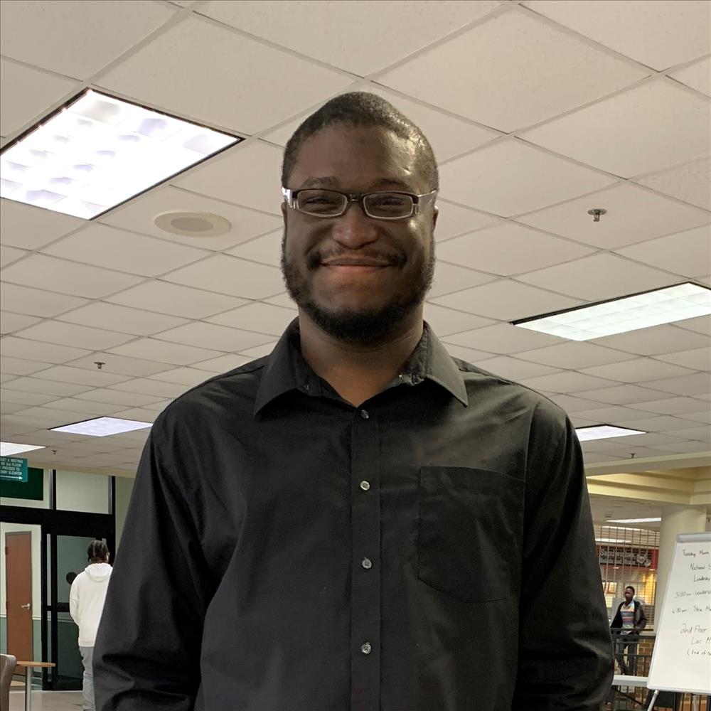 Rashad Brooks smiling wearing all black business attire.