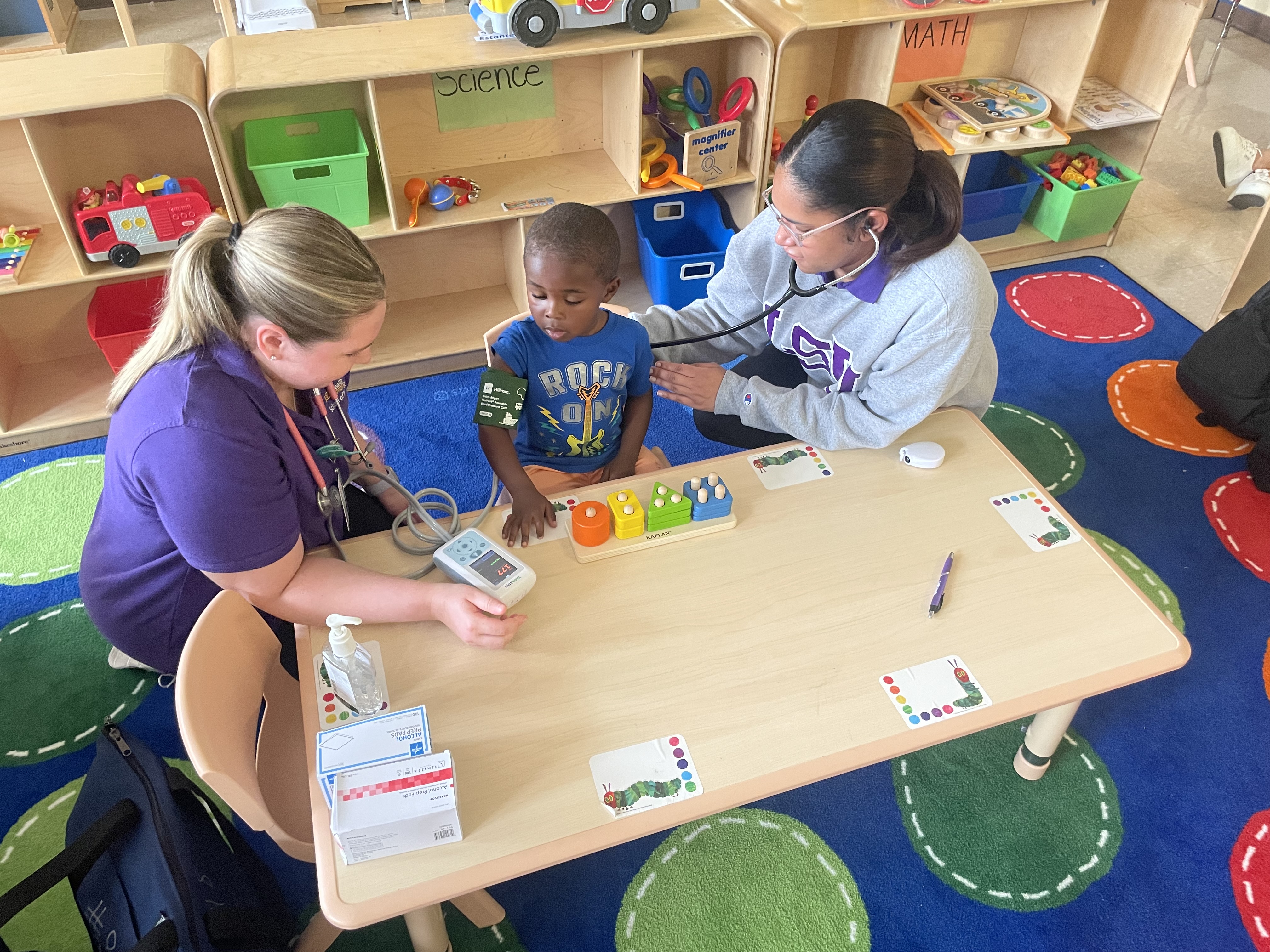 Two LSUHSC students take toddler's blood pressure in his classroom.