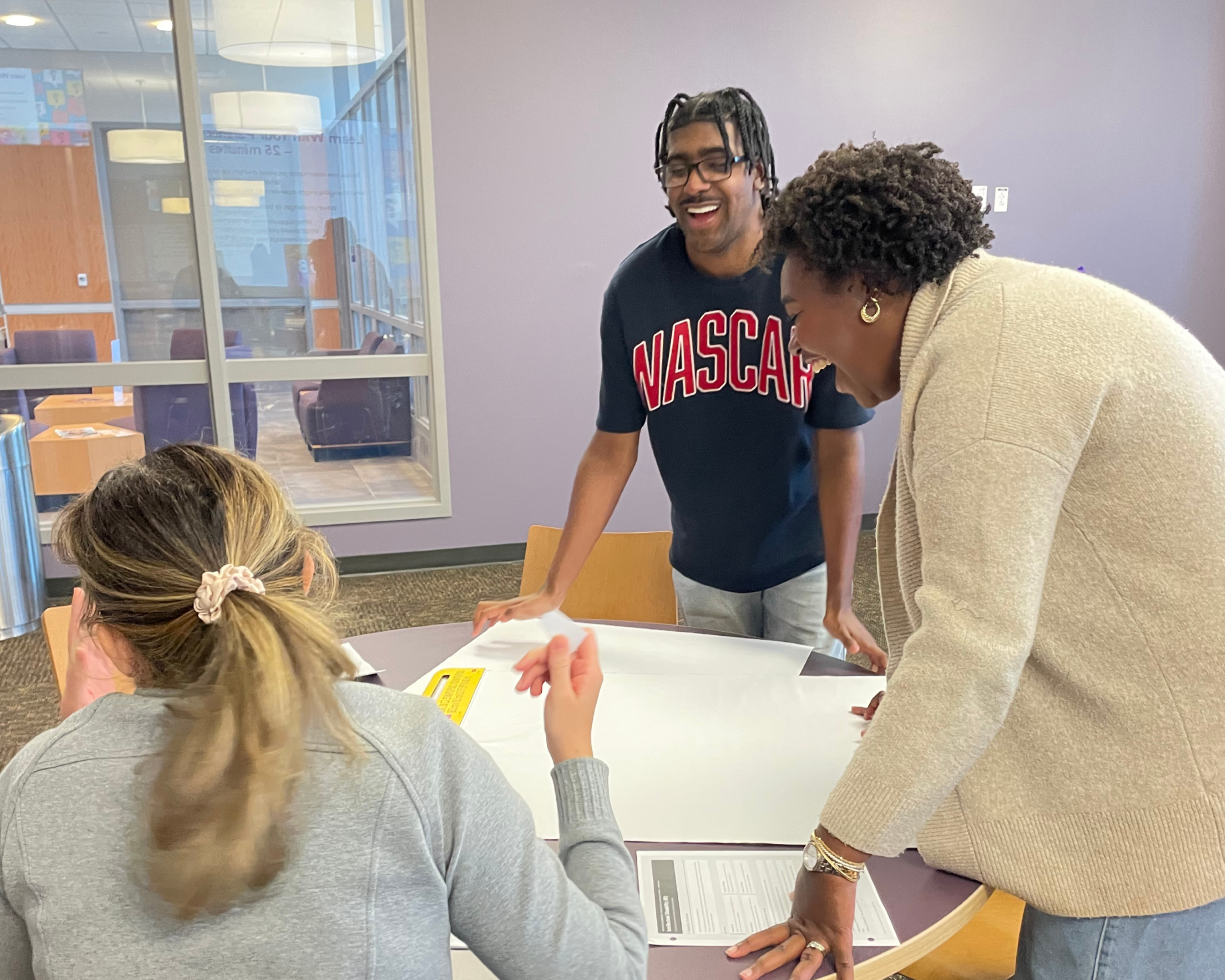 Three scholars smile and laugh as they work on group project together.